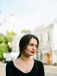 Portrait of young woman in city against sky