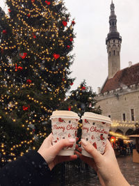 Cropped hands of woman holding disposable cups against christmas tree