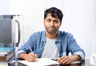 An indian young male looking worried and thinking while studying at home on white background