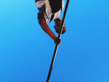 Low angle view of man holding rod against clear blue sky