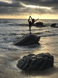 People standing on rock by sea against sky during sunset