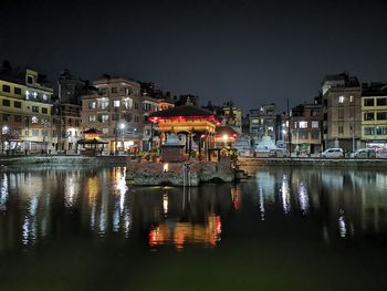 Illuminated buildings by lake against sky in city at night