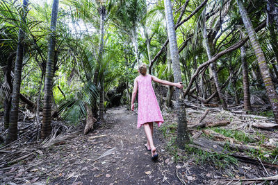 Rear view of girl walking on field amidst trees in forest