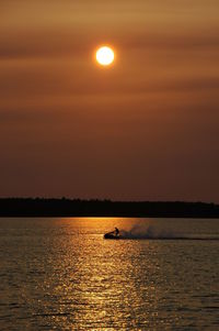 Silhouette person on jet boat over lake against sky