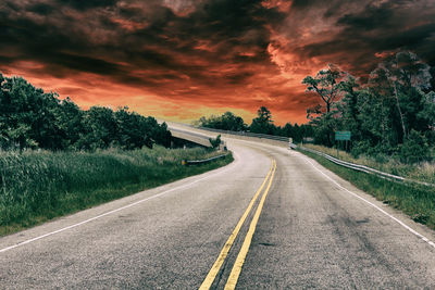 Road by trees against sky during sunset