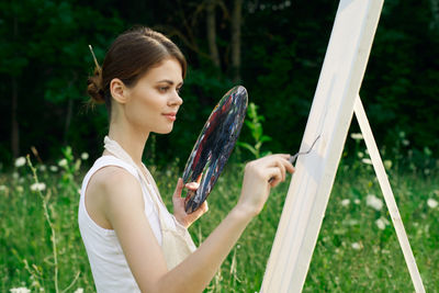 Young woman holding umbrella while standing on field