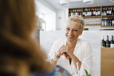 Happy blond woman sitting with friend in restaurant