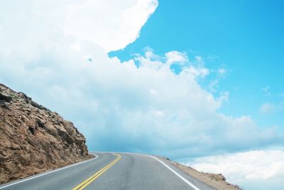 Empty road by mountain against cloudy sky