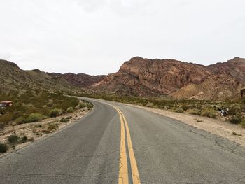 Empty road amidst rocky mountains against clear sky