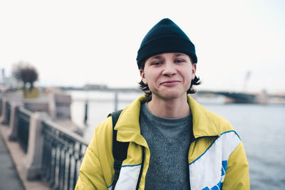 Handsome guy teenager boy 18-19 year old wear knit hat and trendy winter jacket posing at city view