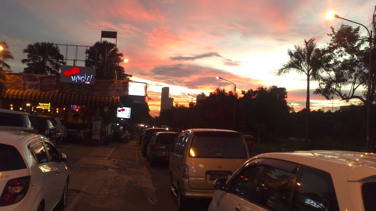 sunset, car, transportation, land vehicle, mode of transport, sky, building exterior, tree, street, architecture, orange color, cloud - sky, built structure, city, road, traffic, silhouette, city street, street light, dusk