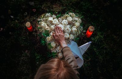 High angle view of woman touching heart shape flower at cemetery