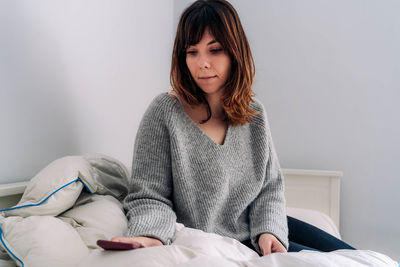 Beautiful young woman sitting on bed at home