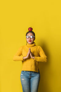 Portrait of young woman standing against yellow background