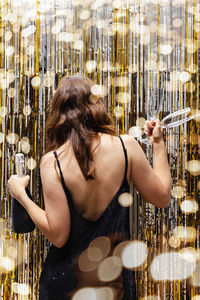 Woman entering new year party with bottle of champagne and glasses in her hands. 