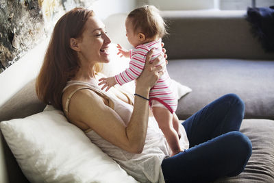 Mother playing with daughter while sitting on sofa at home