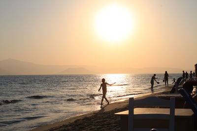 Silhouette people on beach against sky during sunset