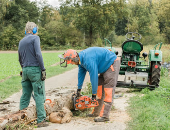 Men cutting log on footpath in forest