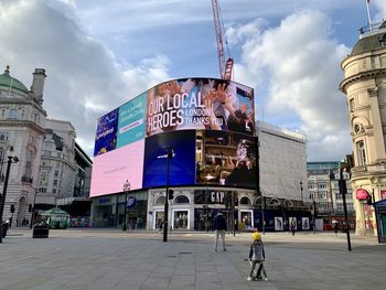 People on street in city against cloudy sky