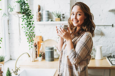 Portrait of smiling woman holding coffee cup standing at home