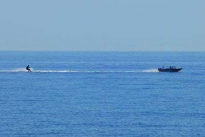 Mid distance view of person wakeboarding on sea against clear blue sky during sunny day