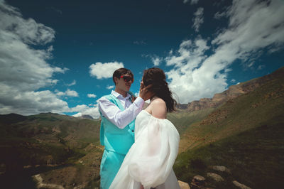 Beautiful wedding couple laughs and plans to kiss against the backdrop of mountains and cloudy sky