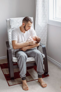 Full length of man holding baby girl while sitting on chair at home