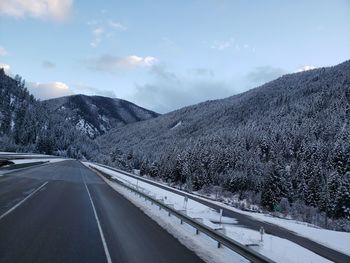 Road by mountains against sky during winter