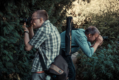 Side view of friends photographing while standing in forest