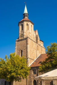 Low angle view of trees and building against blue sky