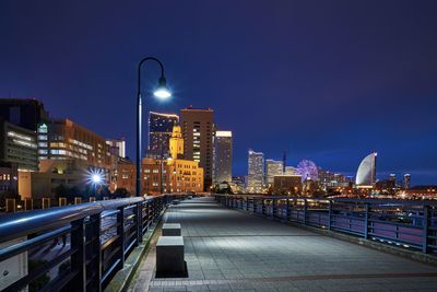 Illuminated street amidst buildings against sky at night