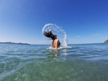 Woman tossing hair in sea against clear sky