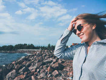 Smiling woman wearing sunglasses standing at beach against sky