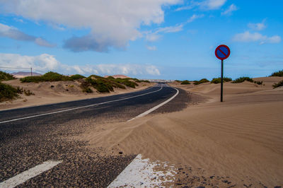 Road sign by land against sky