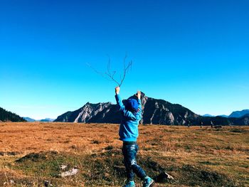 Rear view of boy holding stick while walking on land against clear sky