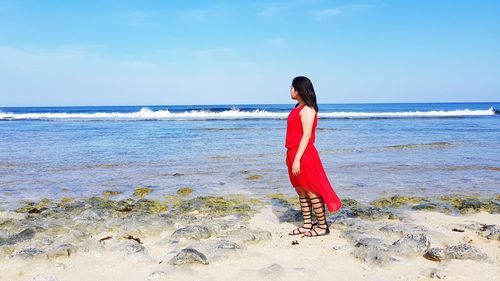 Rear view of woman standing at beach against sky