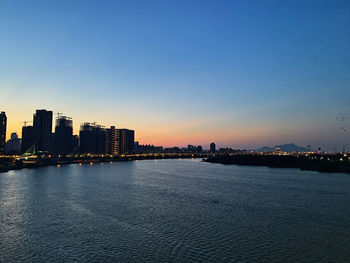 Sea by buildings against clear sky during sunset