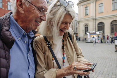 Happy senior couple sharing smart phone while exploring city