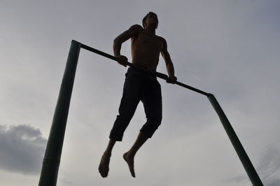 Low angle view of shirtless man performing acrobatics against sky