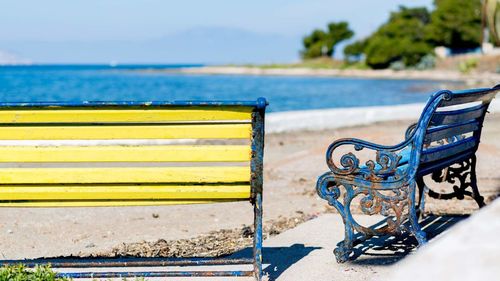 Empty bench on beach by sea against sky