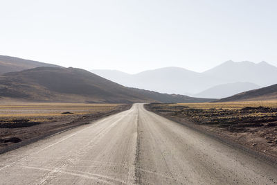 Empty road leading towards mountains against sky