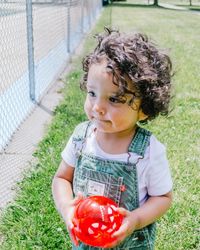 Baby boy holding ball looking away in park