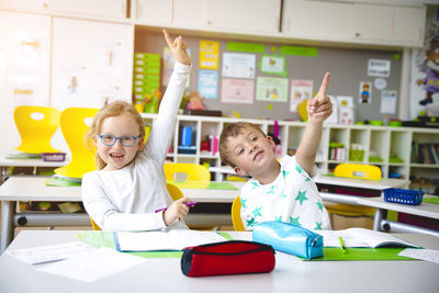 Boy and girl with hands raised at table in classroom