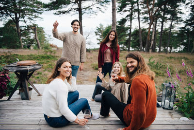 Portrait of happy friends enjoying drinks while sitting on steps at patio