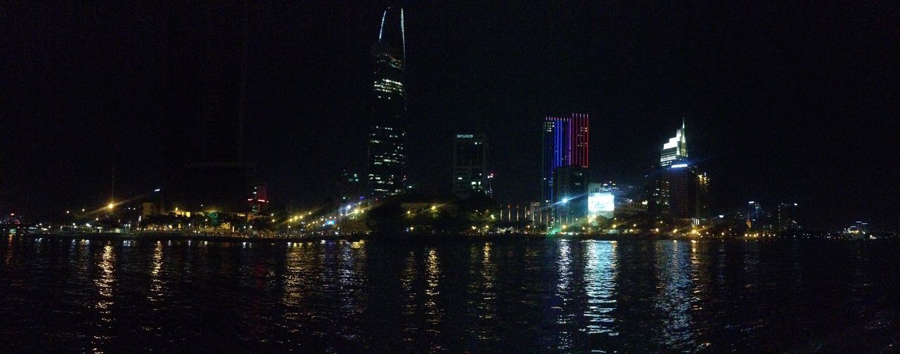 ILLUMINATED BUILDINGS BY RIVER AGAINST SKY