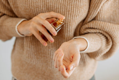 Midsection of woman spraying perfume on hand