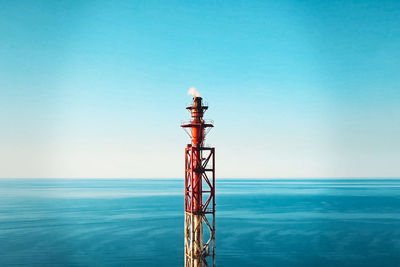 Tower by sea against clear blue sky