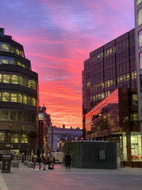 People walking on street amidst buildings against sky during sunset