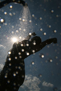 Low angle view of silhouette woman taking shower against sky
