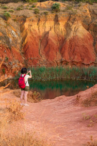 Rear view of woman taking a picture of a green lake born on an abandoned bauxite mine